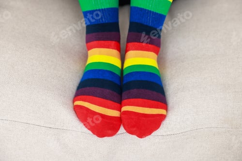Preview: Woman wearing socks in LGBT colors on sofa indoors, closeup