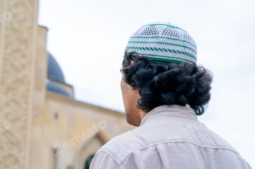 Preview: Back shot of Arab man entering the inner courtyard a mosque on a terrace with Islamic ornamentation