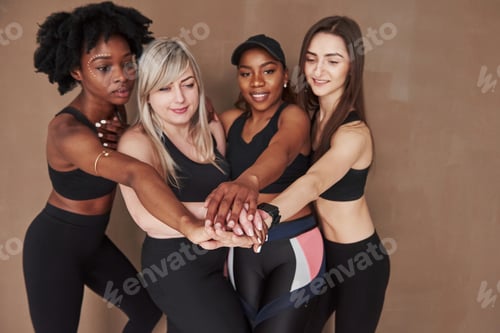 Preview: Pre workout ritual. Group of multi ethnic women standing in the studio against brown background