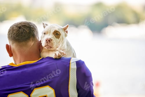 Preview: American football player with a dog posing on camera in a park. Copy space, sports banner. Concept