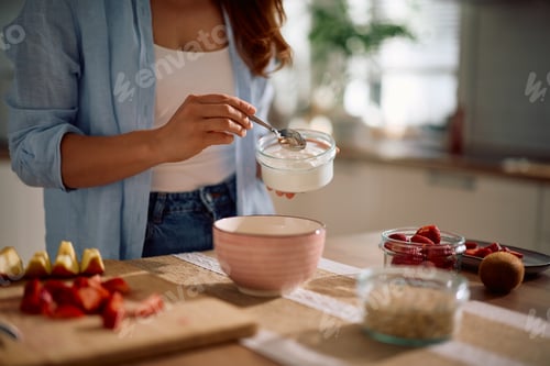 Preview: Close up of woman adding non fat yogurt while making healthy breakfast at home.
