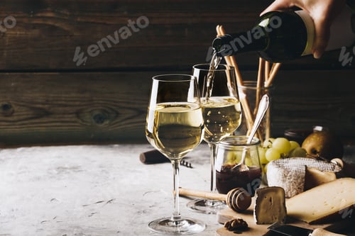 Preview: White wine pouring into glasses with charcuterie assortment on t