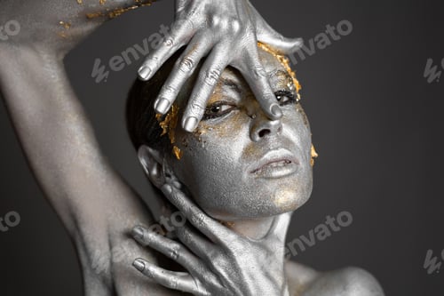 Preview: Portrait of a beautiful female model with gold and silver paint on her skin and hair in the studio