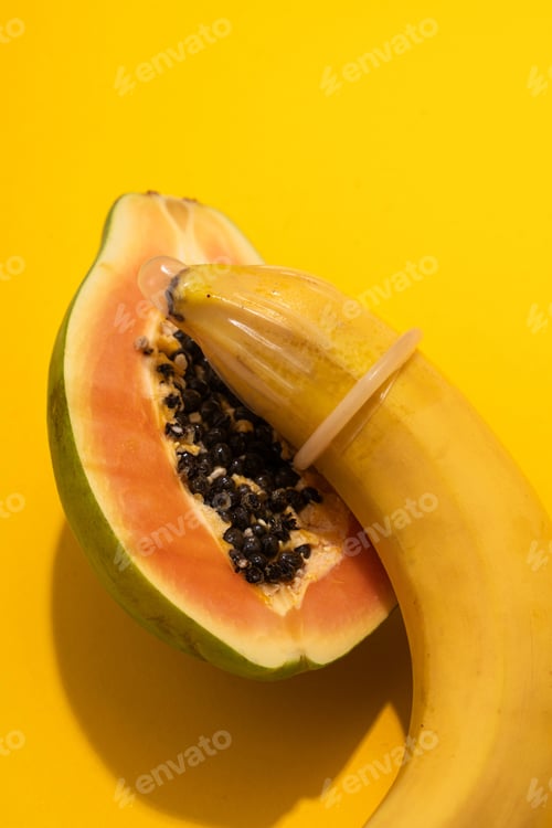 Preview: Banana with Condom and Papaya on yellow background. Sexual Health and Education Concept