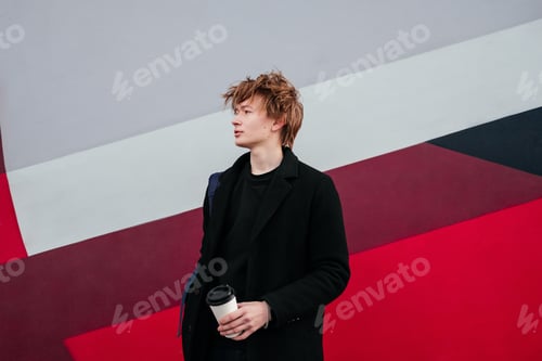 Preview: Thinking young man in black coat with cup of coffee in hands