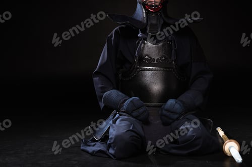 Preview: Partial view of kendo fighter in helmet with bamboo sword sitting on black