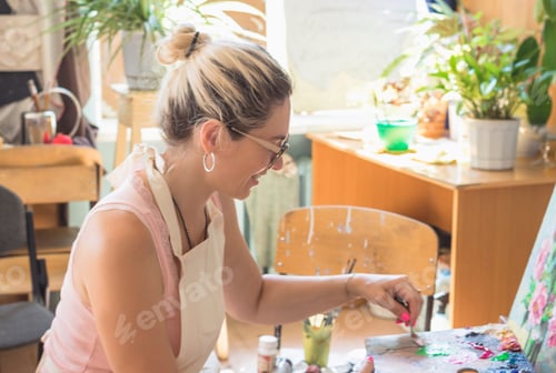 Preview: Beautiful stylish woman artist sits behind a canvas and paints a picture