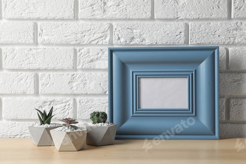 Preview: Blank frame and succulent plants on wooden table near white brick wall, space for design. Home decor