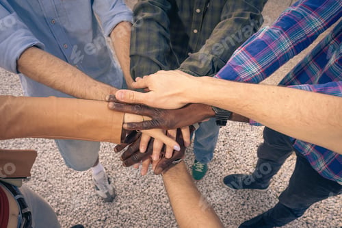 Preview: Top view of diverse people stacking their hands together in a show of unity.