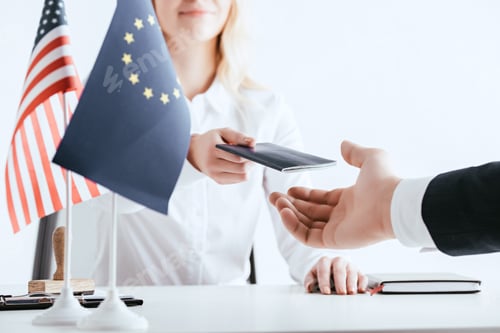 Preview: cropped view of woman giving passport to tourist near american and european flags isolated on white