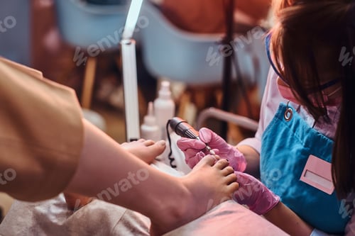 Preview: Young cheerful nail master is working on client's toe nails at her pedicure studio.