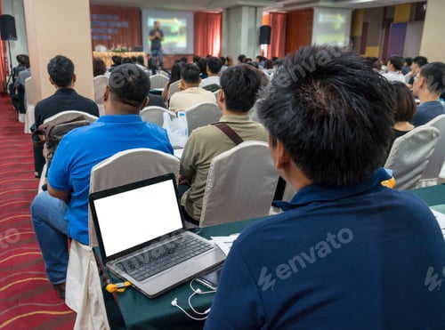 Preview: Speakers on the stage with Rear view of Audience using the technology laptop for shot note