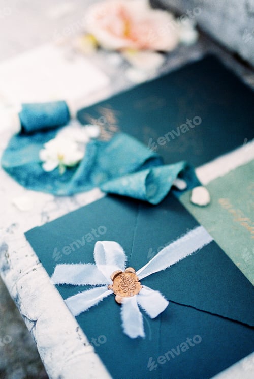 Preview: Navy blue wedding envelope with a ribbon and a wax seal lies on a tile