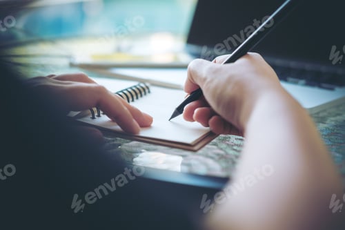 Preview: A woman working and holding black pencil and writing on notebook on glass table