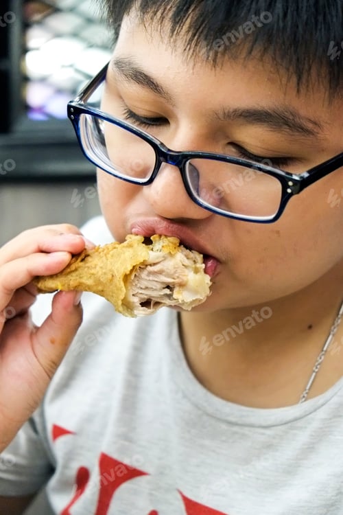 Visualização: Retrato de close-up de uma criança asiática adolescente comendo coxa de frango frito