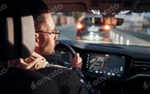 Preview: Rear view of handsome unshaved man in fashionable clothes that riding his automobile