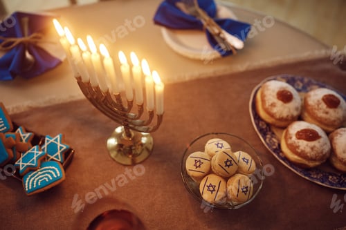 Preview: Close up of traditional Hanukkah table setting with lit candles in menorah.