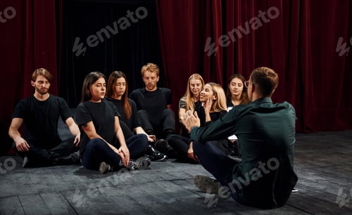 Preview: Sitting on the floor. Group of actors in dark colored clothes on rehearsal in the theater