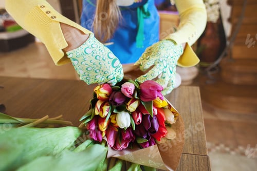 Preview: Girl florist is packing beautiful tulips in a flower shop in kraft paper.