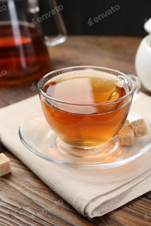 Preview: Aromatic black tea in glass cup, brown sugar and teapot on wooden table, closeup