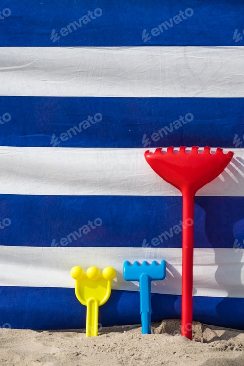 Preview: Colorful childrens beach toys in a sand in front of a wind scree