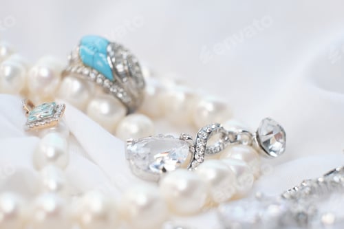 Preview: Close-up of elegant jewelry pieces, including pearls, silver rings, and a blue gemstone ring on a