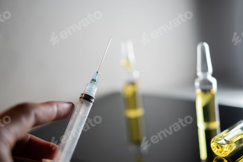 Preview: Syringe and vials of yellow liquid on reflective surface