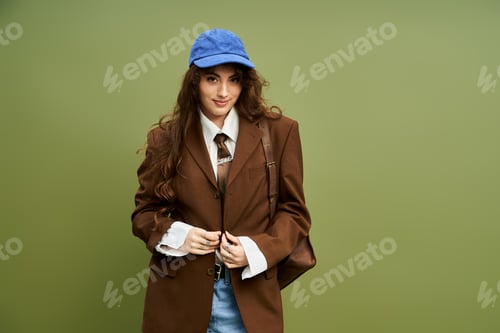 Preview: Stylish young woman looks confidently at the camera in a chic outfit in front of a green background