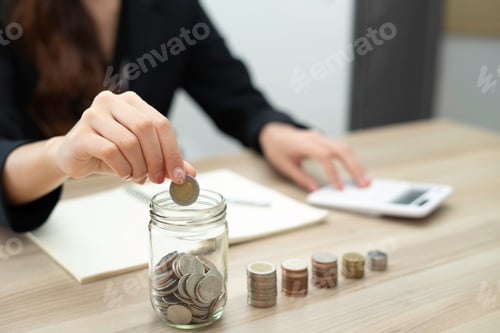 Preview: A close-up picture of a business woman putting a coin in a glass jar To save money and plan for it a