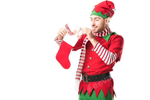 Preview: man in christmas elf costume putting present in red christmas stocking isolated on white