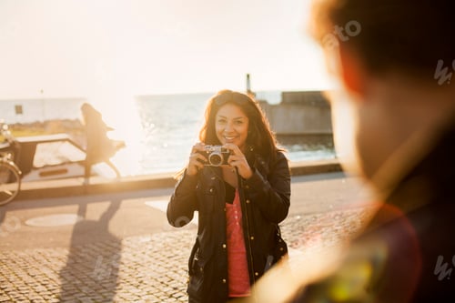 Preview: Portrait of happy young woman photographing friend against sea on sunny day