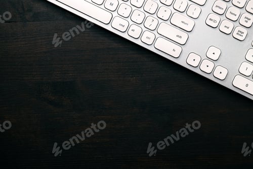 Preview: Modern white aluminum computer keyboard on dark wooden home office desk as copy space