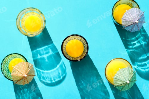 Preview: shot from above of glasses filled with orange juice illuminated with hard light on blue background
