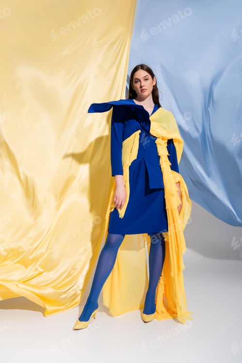 Preview: full length of young ukrainian woman in fashionable color block clothing posing near blue and yellow