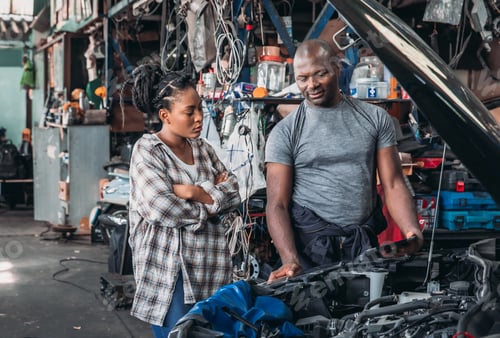 Preview: Mechanic Explains Car Repairs to a Woman in a Busy Workshop During the Day
