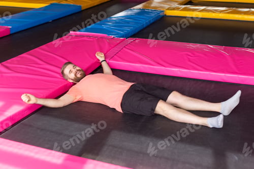 Preview: Fitness, fun, leisure and sport activity concept - Man lying on a trampoline indoors, top view