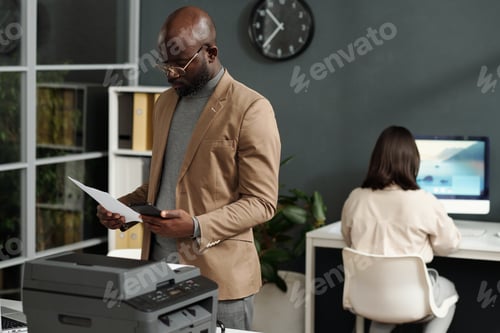 Preview: Young serious African American ceo comparing data in smartphone and on paper