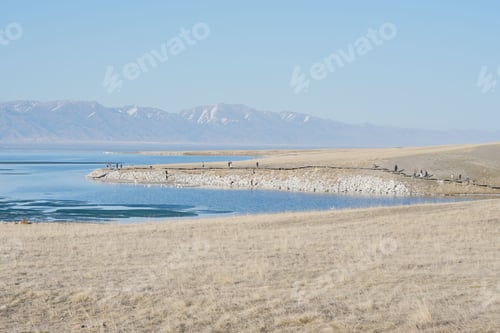 Preview: Scenic view of people on shoreline against a sea and a mountain range