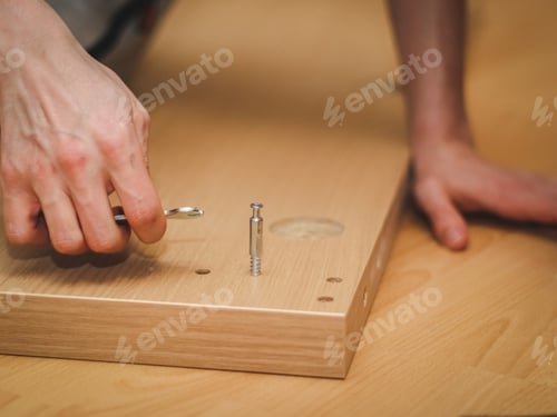 Preview: The hands of a caucasian young man with a wrench tighten a bolt on the wooden part of the bed