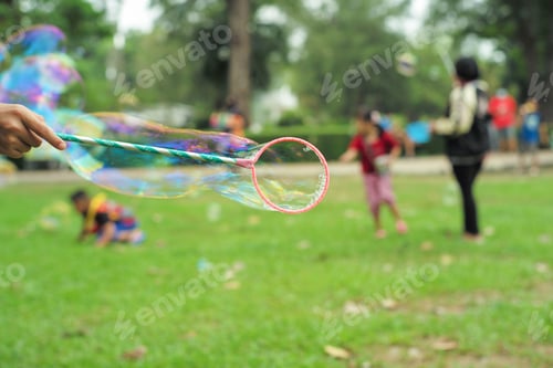 Preview: Hand holds the plastic ring for making bubble from soap with blurred group of people playing at the