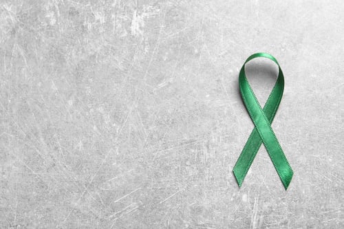 Preview: Green ribbon on grey background, top view. Cancer awareness