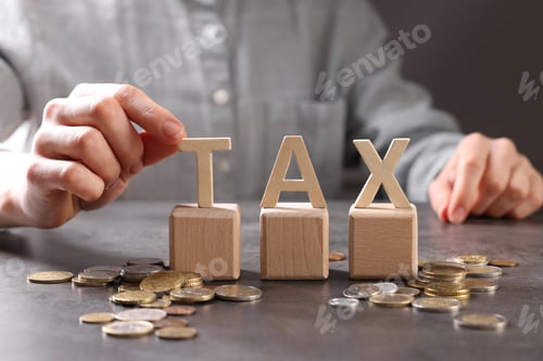 Preview: Woman with word Tax, wooden cubes and coins at grey table, closeup