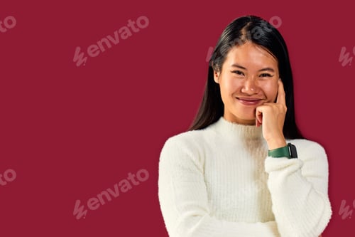 Preview: Portrait of a happy Asian woman, with a hand on her head, in front of the red wall.