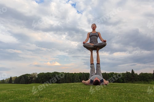 Preview: Young couple doing acro yoga in park. Man lying on grass and balancing woman in