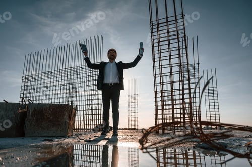Preview: With hands up. Standing at evening time. Businessman in formal clothes is on the construction site