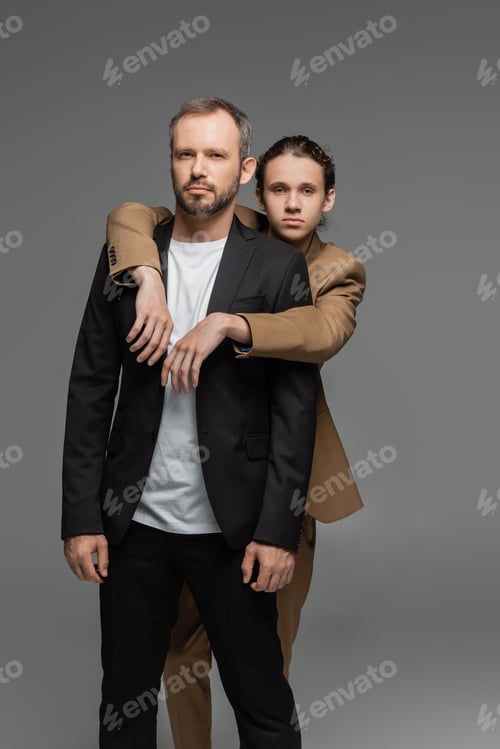 Preview: well dressed teenage boy hugging father in suit isolated on grey