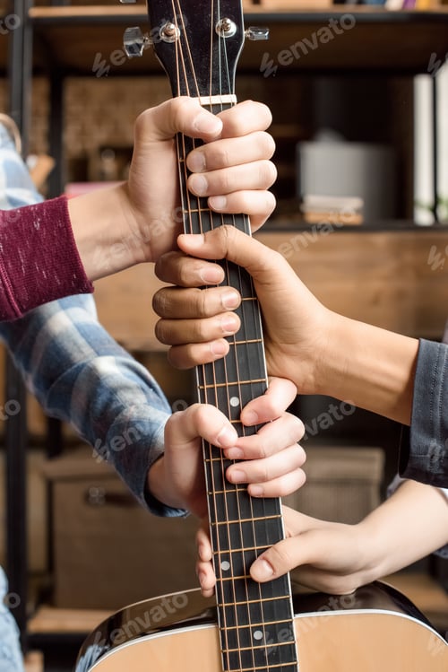 Preview: cropped view of teenagers holding guitar fretboard at home, teenagers playing guitar concept