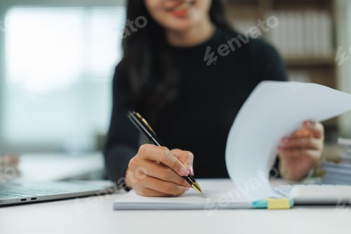 Preview: Businesswoman taking notes and reading documents at office desk