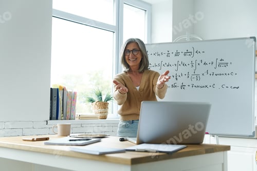 Preview: Happy senior woman gesturing while standing near the whiteboard at classroom