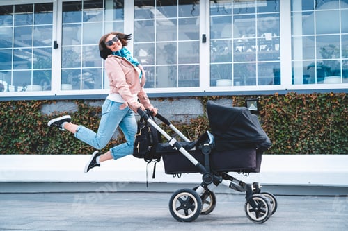 Preview: Happy woman young mother jumping with stroller on the street